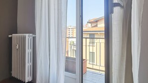 A room with a radiator, white curtains, and a view of buildings through a window. - Italianway Easy - Lecchi 20 (Milan)