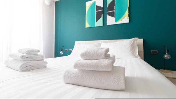 A neatly made bed with white linens and towels, teal walls, and modern artwork. - Italianway Easy - Lecchi 20 (Milan)