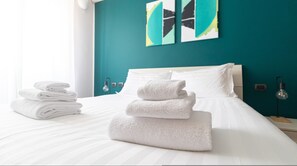 A neatly made bed with white linens and towels, teal walls, and modern artwork. - Italianway Easy - Lecchi 20 (Milan)