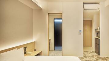 A hotel room with a bed, bedside table, and a small kitchenette area.