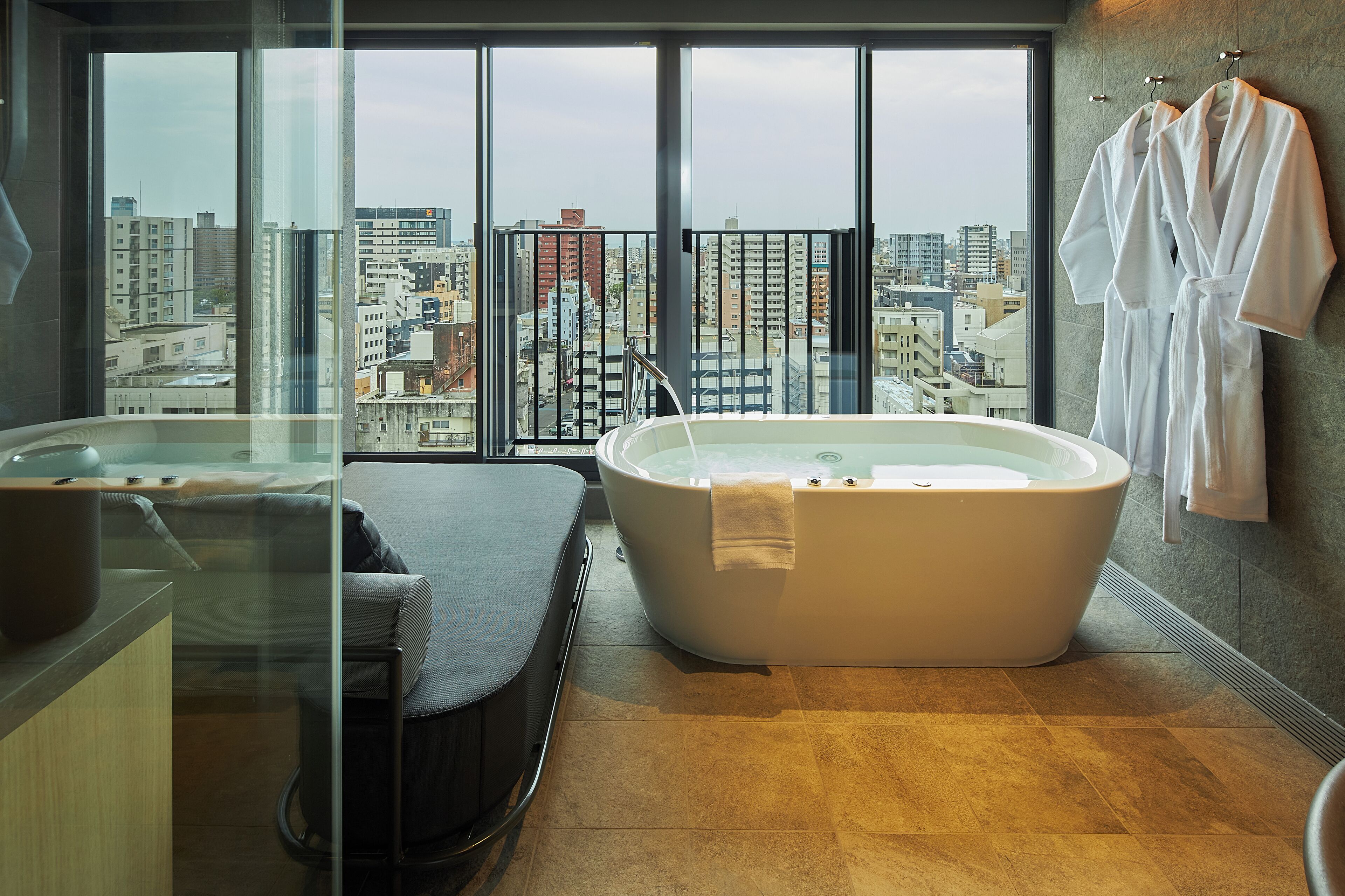 A modern bathroom with a large bathtub, a glass shower enclosure, and a city view through large windows.