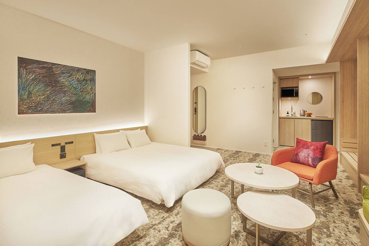 A hotel room with two beds, a small table, a chair, a mirror, and a painting on the wall.