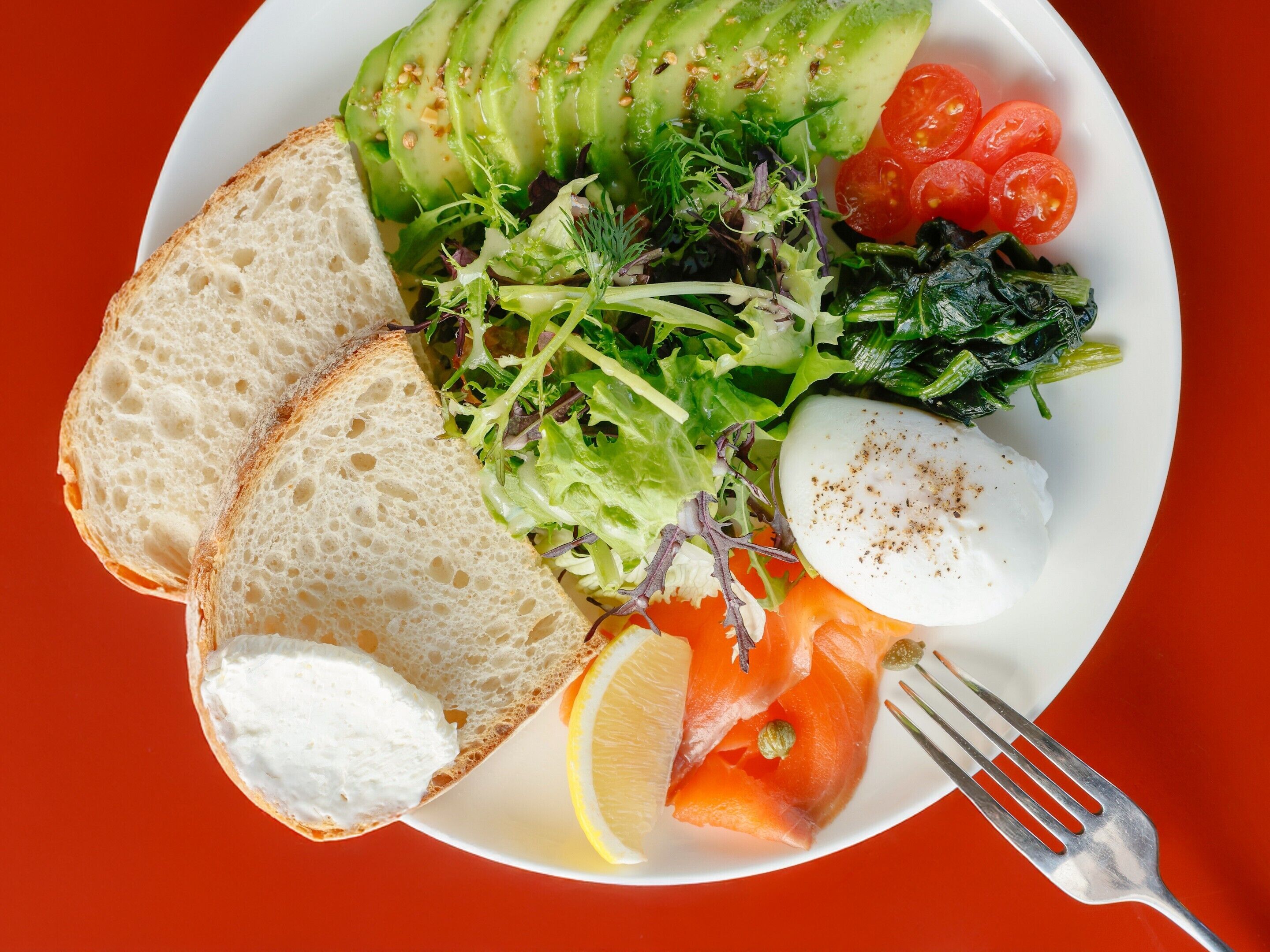 A plate with sliced avocado, cherry tomatoes, leafy greens, a poached egg, and a lemon wedge.
