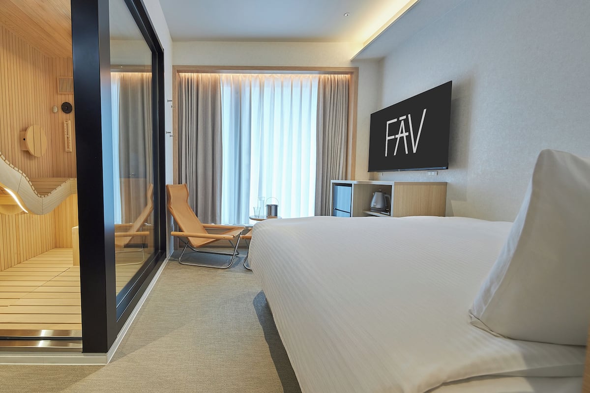 A modern hotel room with a large bed, a TV, a desk, and a chair.