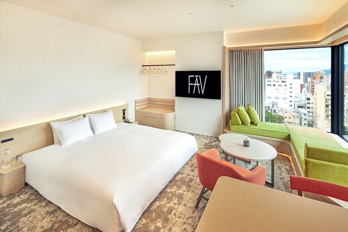 A hotel room with a large bed, a small table, a sofa, and a TV mounted on the wall.