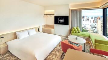 A hotel room with a large bed, a small table, a sofa, and a TV mounted on the wall.