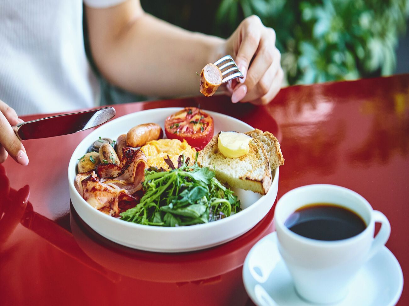 Un plato con huevos, tocino, tomates y verduras acompañado de tostadas y una taza de café.