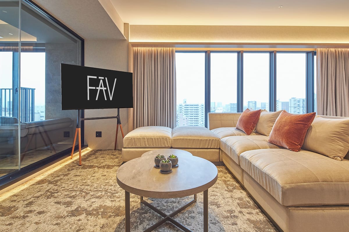 A modern hotel room with a large sofa, a small coffee table, and a TV screen displaying 'FAV'.
