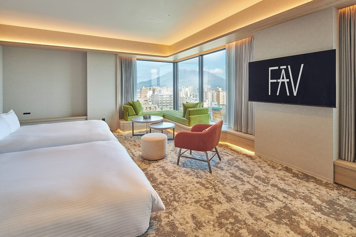 A hotel room with a large bed, two chairs, a small table, and a TV on the wall.