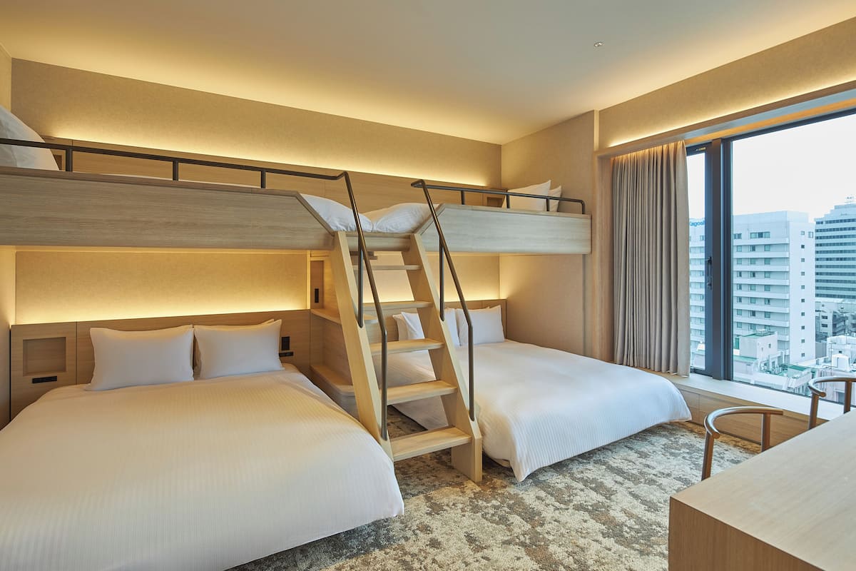 A hotel room with two beds, a wooden ladder, a desk, and a large window with a city view.