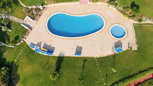 Vista aèria d'una piscina amb un solàrium al voltant, una piscina més petita a prop i una escala que condueix a un edifici.