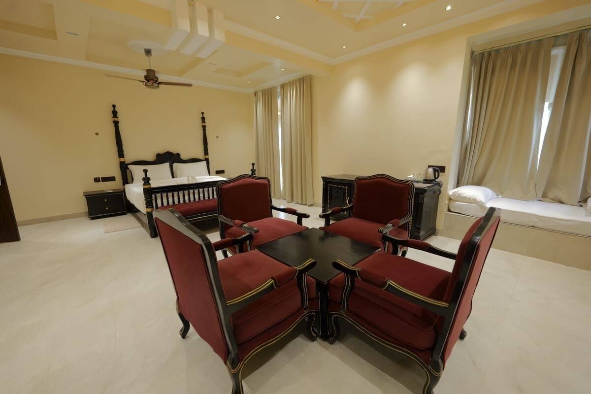 Una habitación amplia con una gran mesa de comedor, cuatro sillas, una cama, una mesita de noche y un ventanal con cortinas.