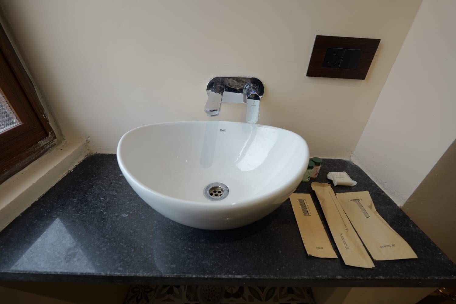 A white vessel sink with a single faucet on a dark countertop, accompanied by a small mirror and some cleaning supplies.