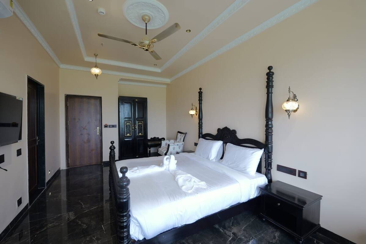 Una habitación de hotel con una cama grande, un ventilador de techo y dos lámparas fijadas a la pared.