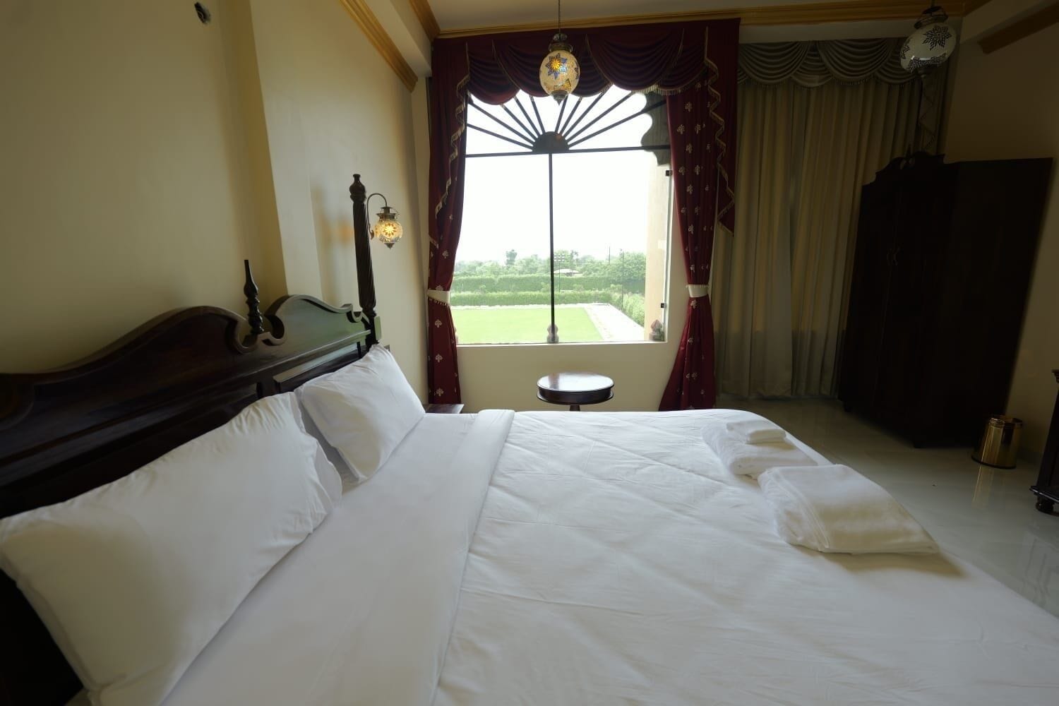 A neatly made bed with white linens, a wooden headboard, and a small round table beside it.