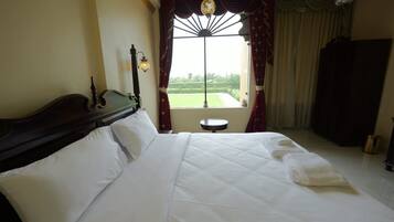 A neatly made bed with white linens, a wooden headboard, and a small round table beside it.