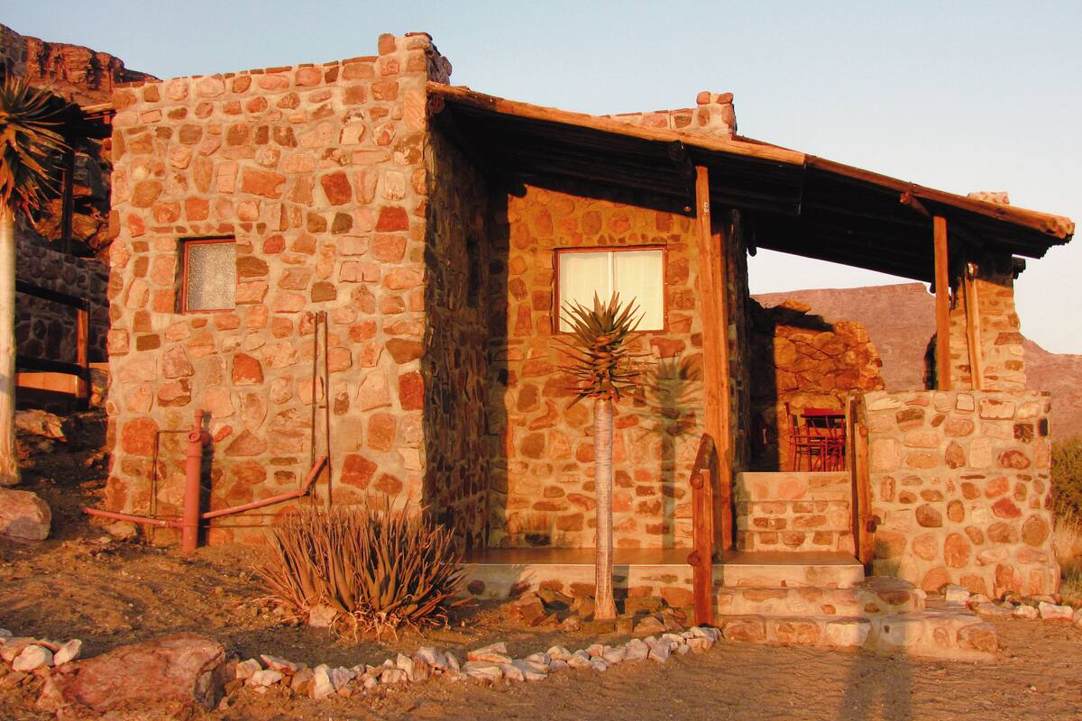 Un bâtiment en pierre doté d’une porte et de fenêtres en bois, entouré de la végétation typique du désert.