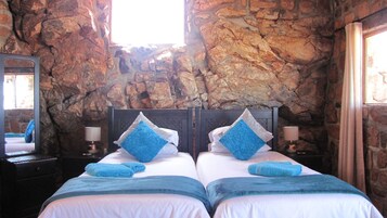 Una cama doble con dos almohadas, una mesita de noche con lámpara y una pared de piedra.