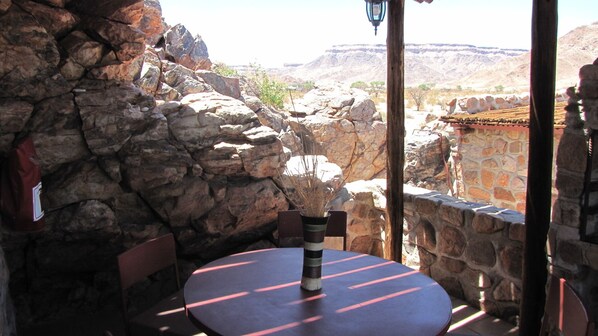 A stone-walled outdoor seating area with a table and chairs, overlooking a canyon.