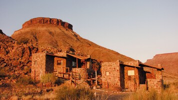 Un edificio de piedra rústico con varias habitaciones, ubicado en un paisaje seco y montañoso.