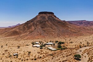 Paisaje desértico con una colina destacada y un pequeño asentamiento con edificios y vegetación escasa.