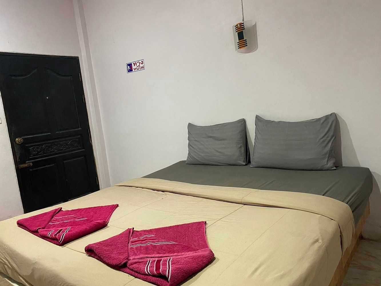 A single bed with a beige bedspread and two pillows, a black door, and a small wall-mounted light fixture.