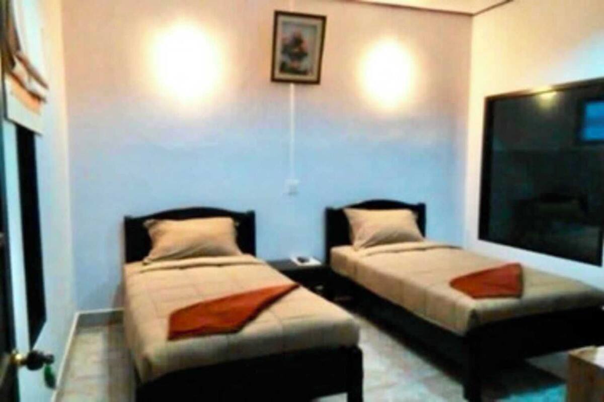 Une petite chambre avec deux lits simples, une grande fenêtre et un tableau accroché au mur.