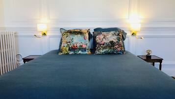 A bed with a dark blue bedspread, two decorative pillows with floral and animal prints, a small bedside table with a lamp, and a wall-mounted light fixture.