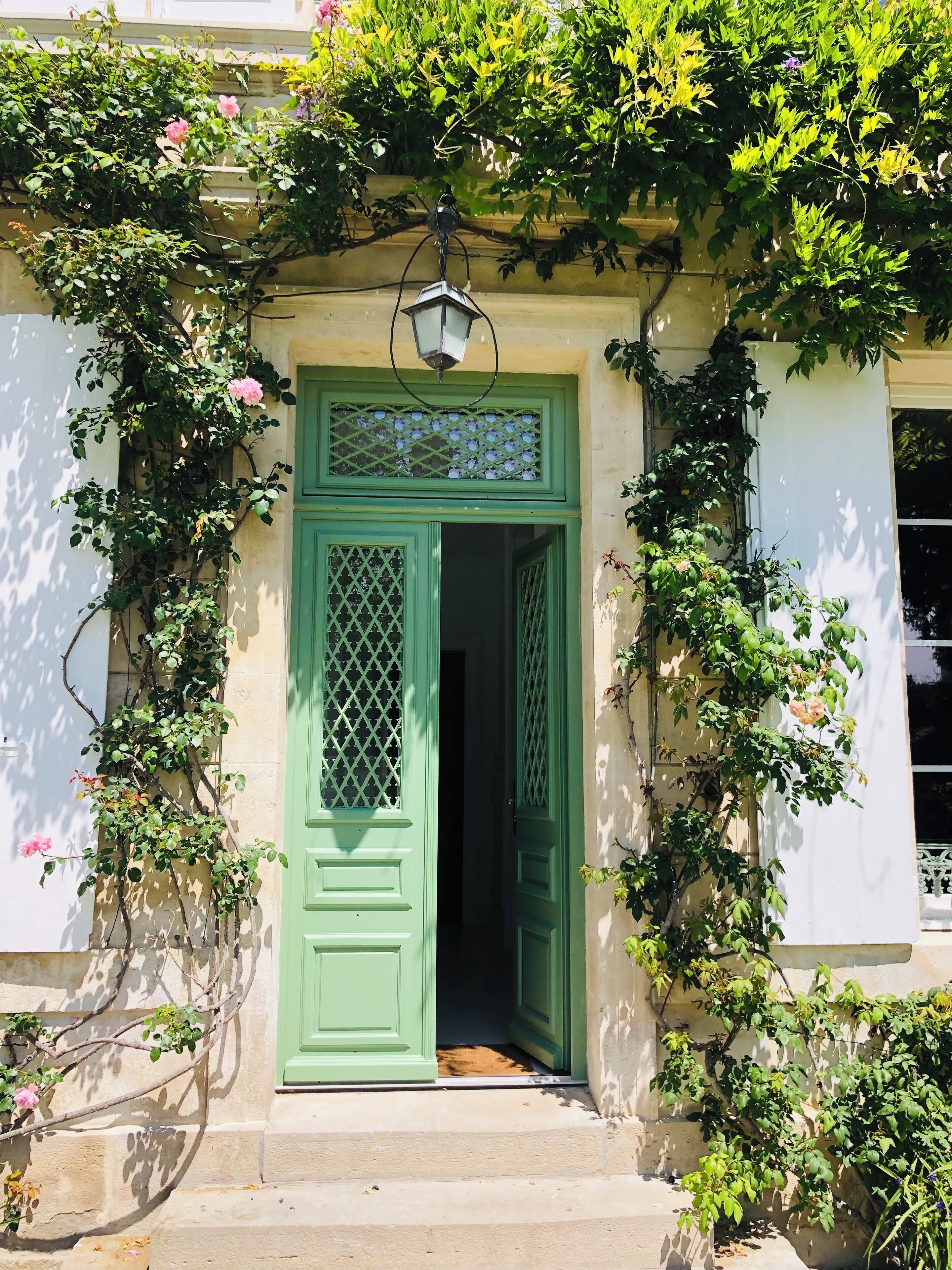 Une porte verte ornée d’un motif en treillis, une petite marche menant à cette porte, et un luminaire placé au-dessus.