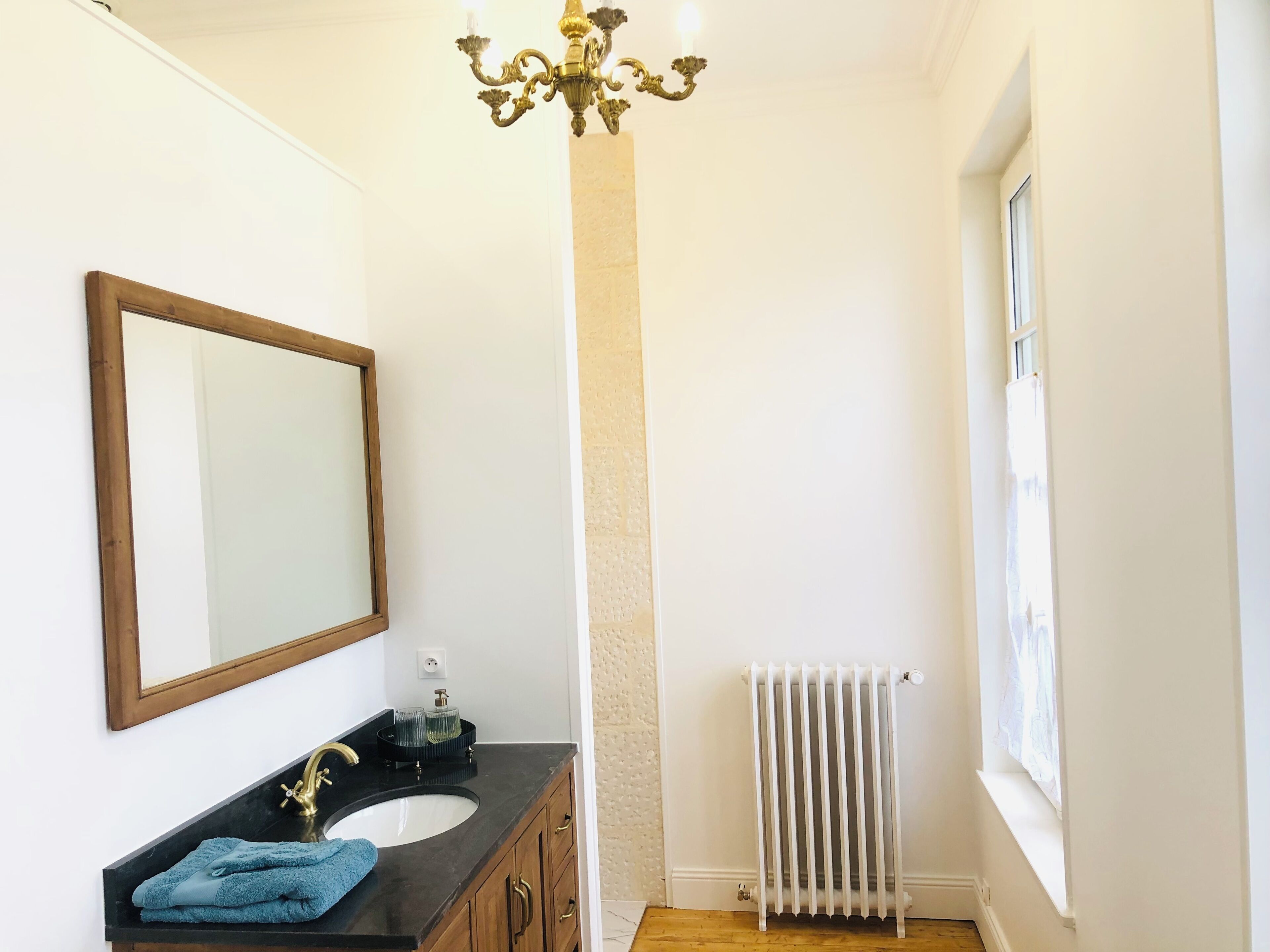 Un baño con tocador de madera, un espejo grande, un radiador blanco y una ventana.