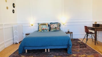 A bedroom with a bed, two wall-mounted lamps, a radiator, a desk with a chair, and a patterned rug.