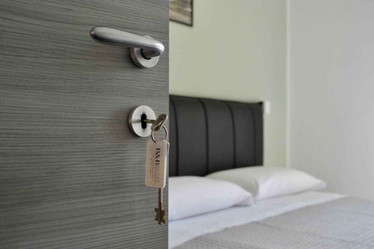 A hotel room with a grey door, a key hanging on the handle, and a bed with white bedding.