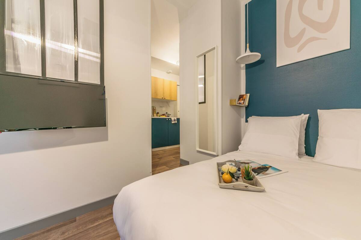 Une chambre avec un lit, un plateau de fruits et de fleurs, et une vue sur une cuisine et un couloir.