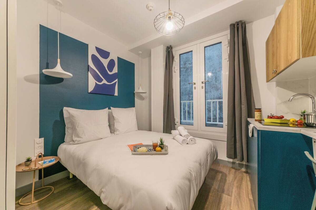 Une chambre d’hôtel moderne équipée d’un lit, d’un plateau de petit-déjeuner, d’une fenêtre avec rideaux et d’une kitchenette.