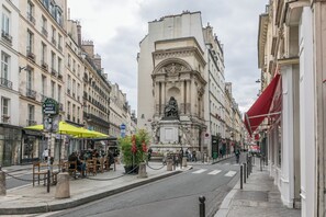 A street with buildings, a statue, and outdoor seating. - WS Louvre - Richelieu (Paris)