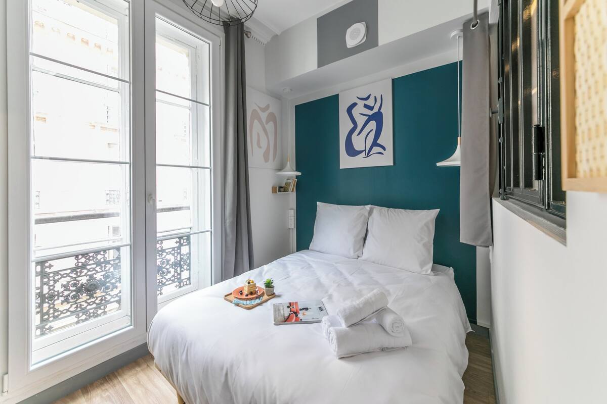 Un lit bien fait, avec du linge de lit blanc, un plateau avec une théière et des tasses, et un livre posé sur le lit.