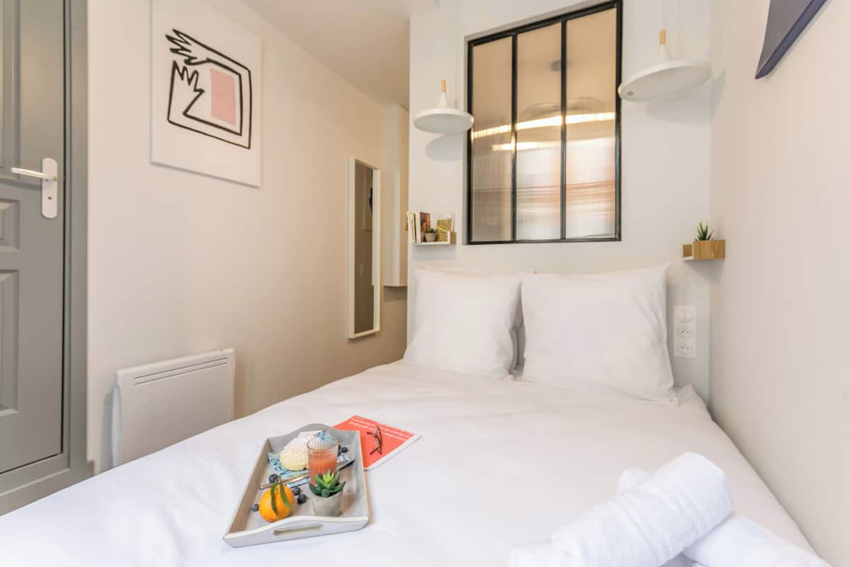 Un lit bien fait, avec du linge de lit blanc, un plateau contenant des articles pour le petit-déjeuner et un tableau encadré accroché au mur.