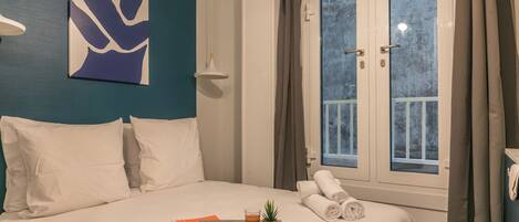 A hotel room with a bed, a tray with food and drink, a window with curtains, and a wall art piece.