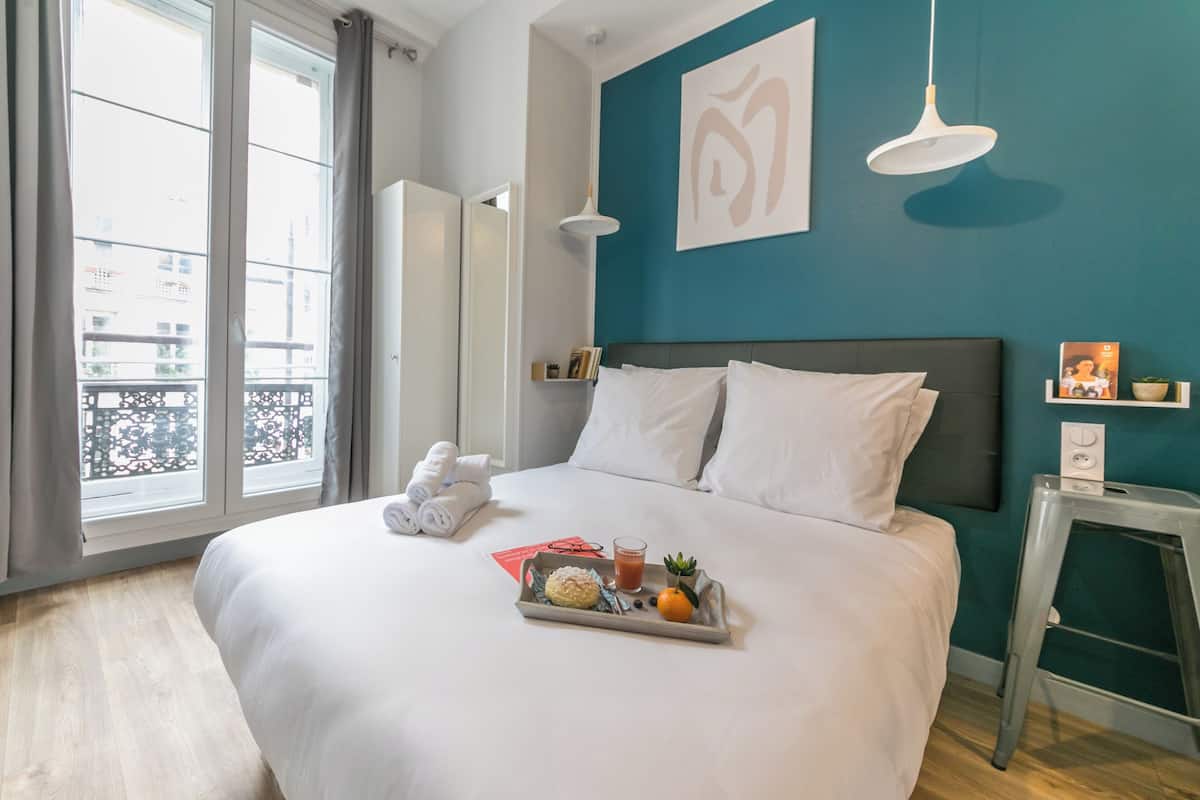 Un lit bien fait, avec du linge de lit blanc, un plateau avec une boisson, un livre et un fruit.