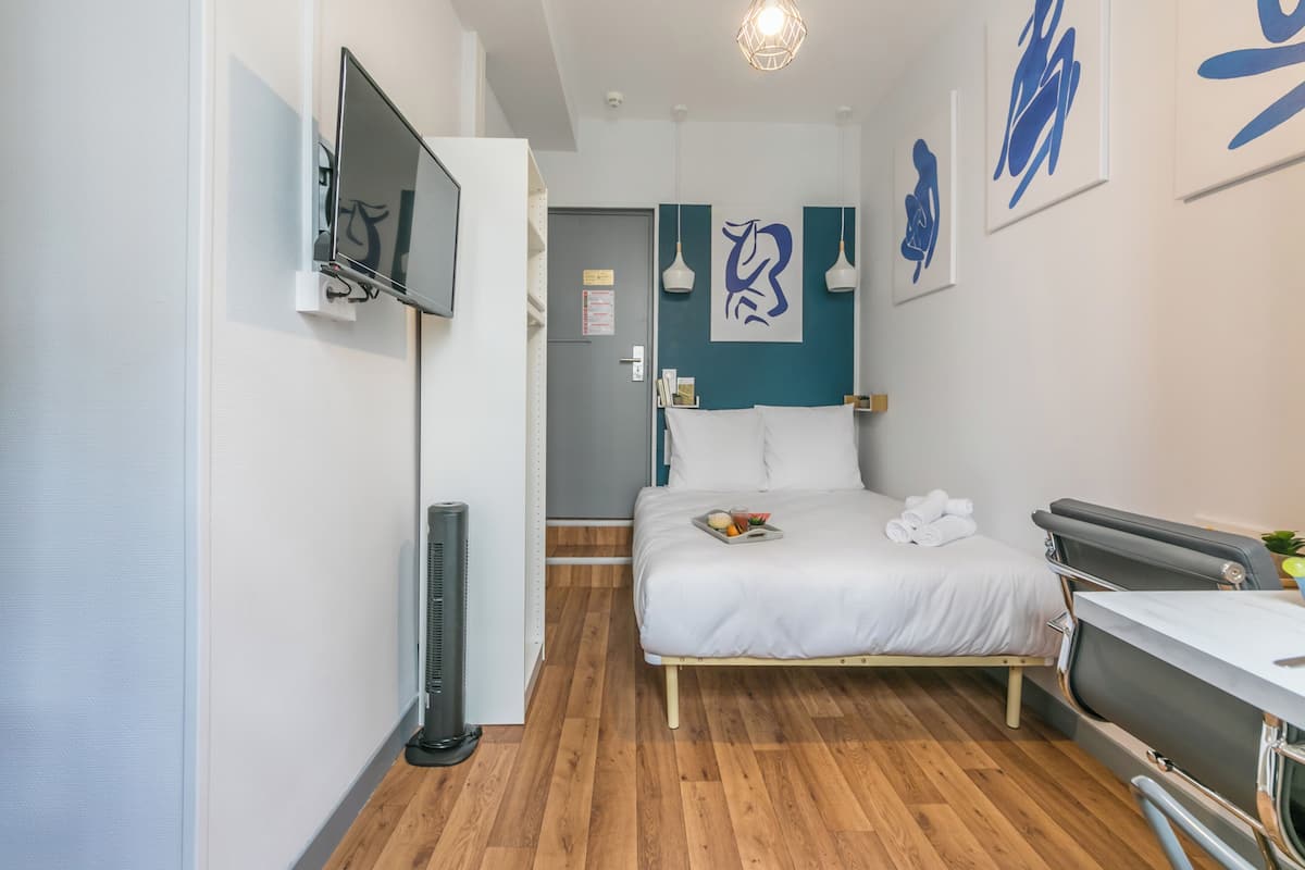 Une chambre d’hôtel moderne équipée d’un lit, d’une table de chevet et d’un téléviseur à écran plat fixé au mur.