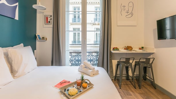 A hotel room with a bed, breakfast tray, and a balcony with a view of buildings. - WS Louvre - Richelieu (Paris)