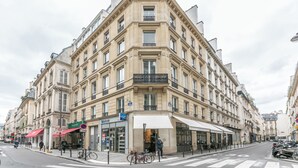 A corner building with multiple stories, storefronts, and a bicycle parked outside. - WS Louvre - Richelieu (Paris)