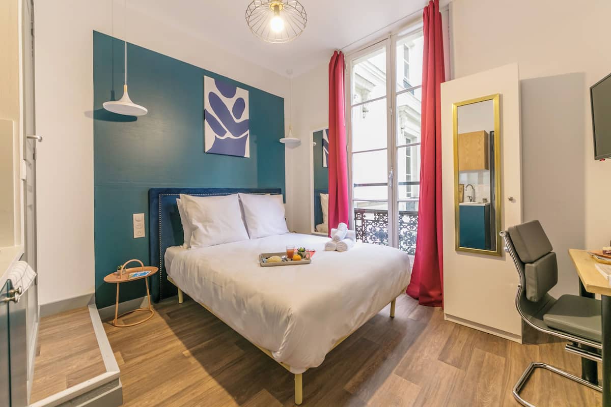 Une chambre d’hôtel moderne avec un grand lit, un bureau et un balcon agrémenté de rideaux rouges.