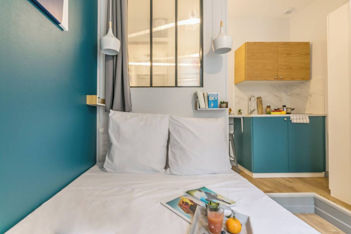 Une chambre d’hôtel de taille réduite, comprenant un lit, une petite kitchenette et une fenêtre avec des rideaux.