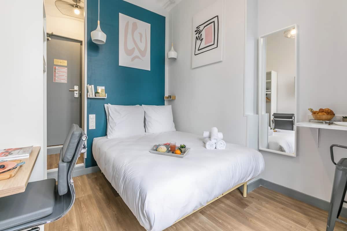 Une chambre à coucher moderne avec un lit, une table de chevet, une chaise et un plateau contenant des fruits et une boisson.