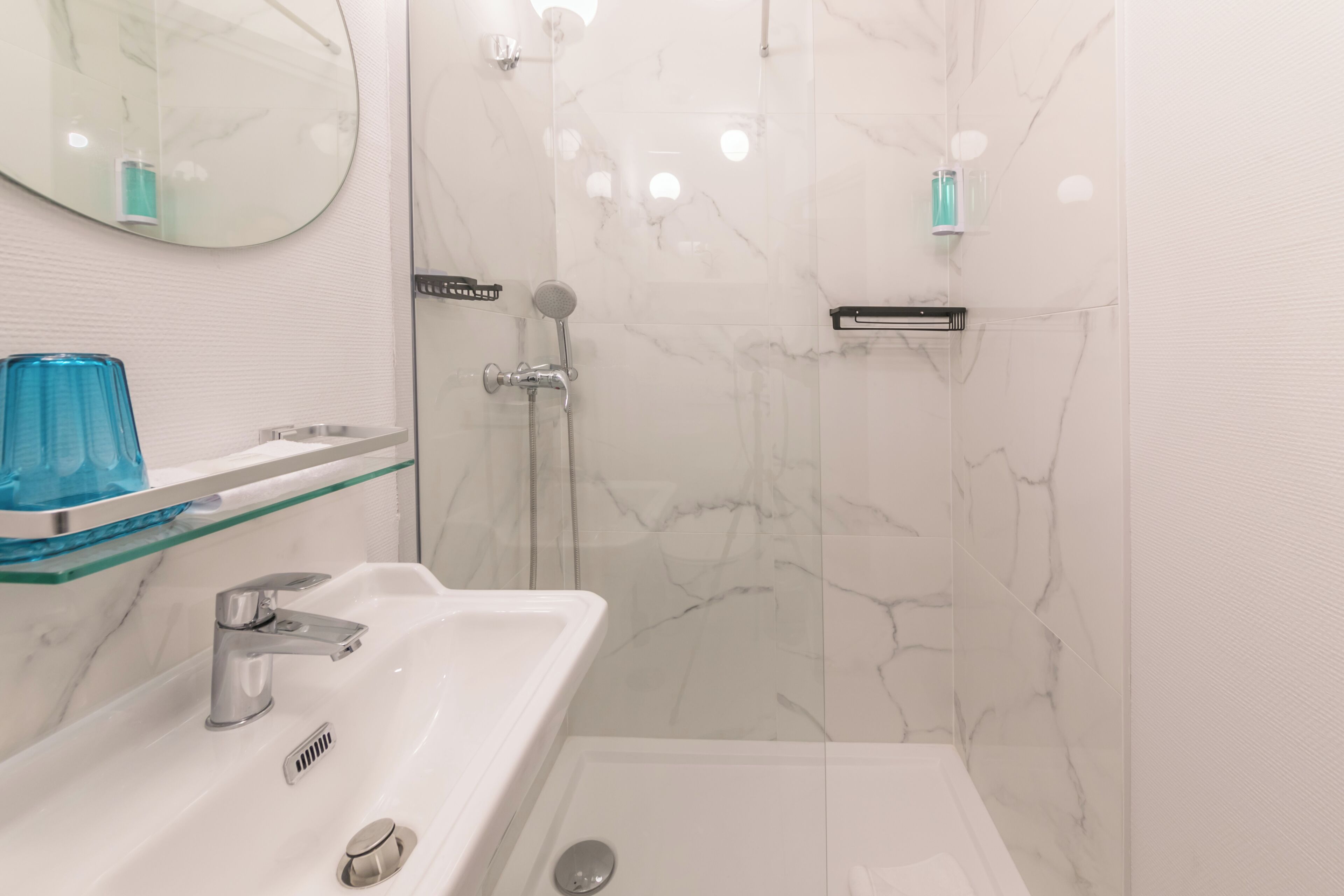 Een moderne badkamer met een witte marmeren douche, een glazen plank met toiletartikelen en een wit wastafelmeubel met een chromen kraan.