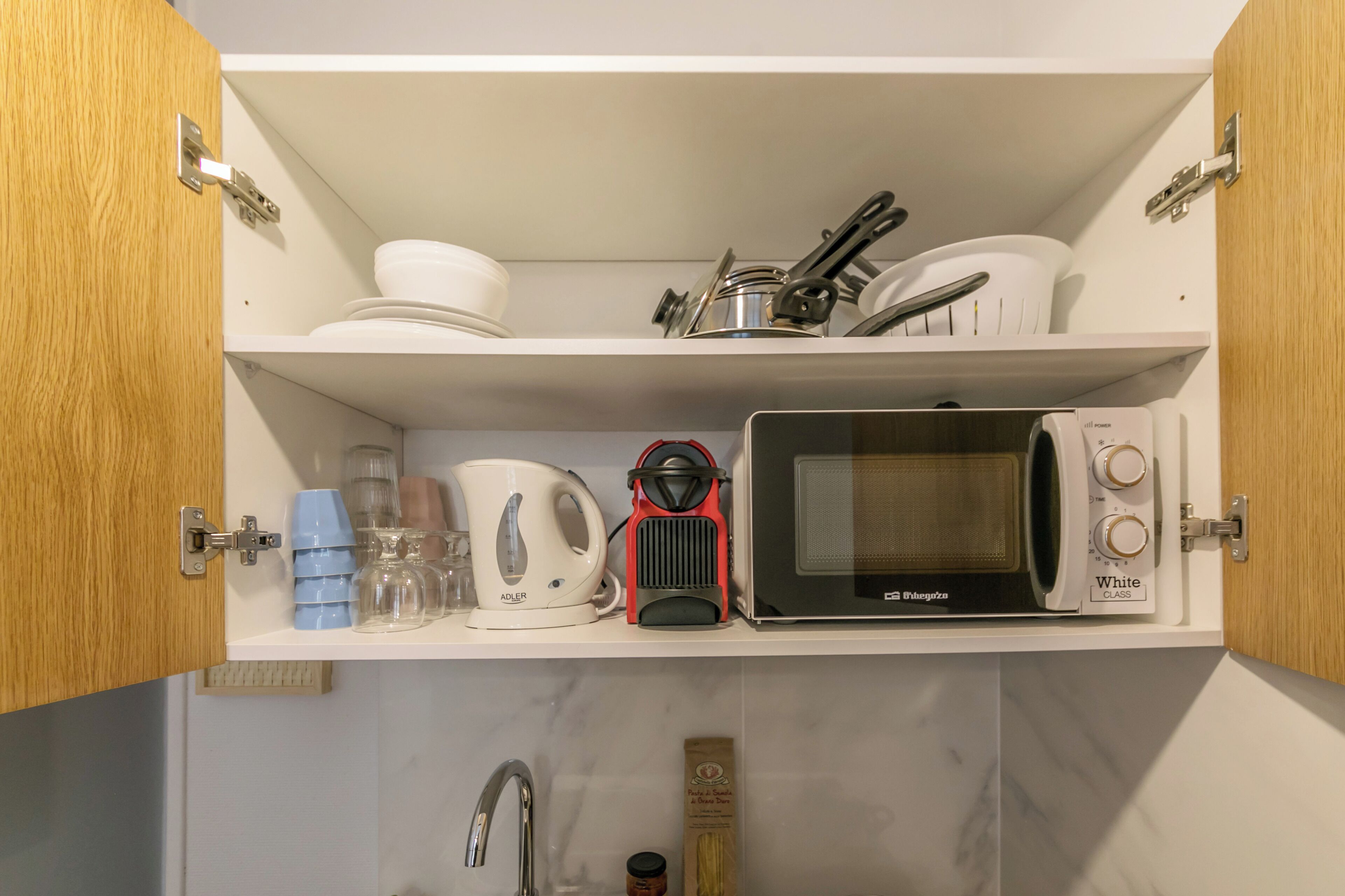 A kitchen with a microwave, kettle, and various kitchen utensils on the shelves.