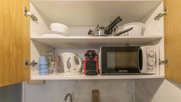 A kitchen with a microwave, kettle, and various kitchen utensils on the shelves.