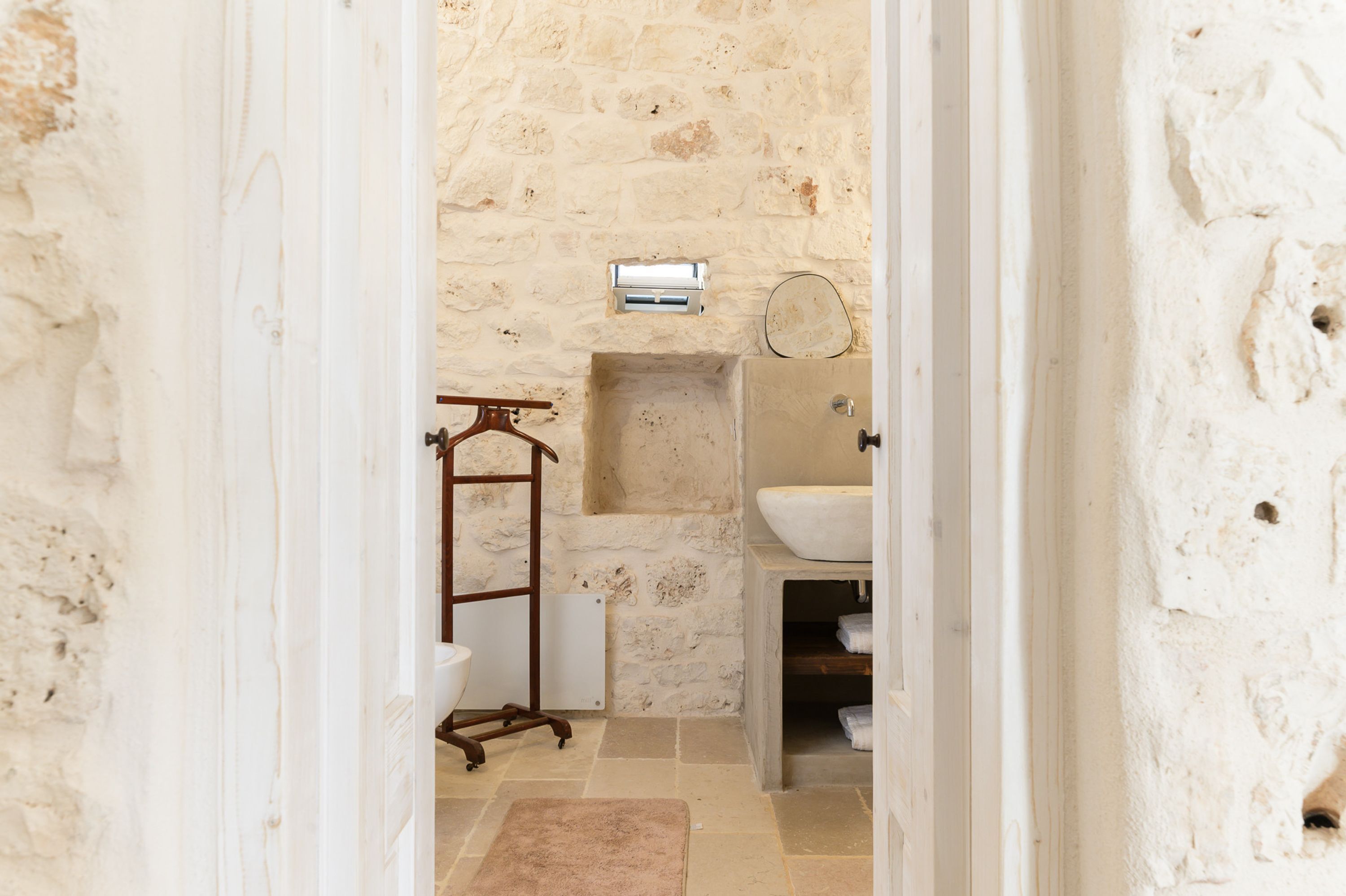 A bathroom with a stone wall, a wooden towel rack, a white sink, and a built-in bathtub.