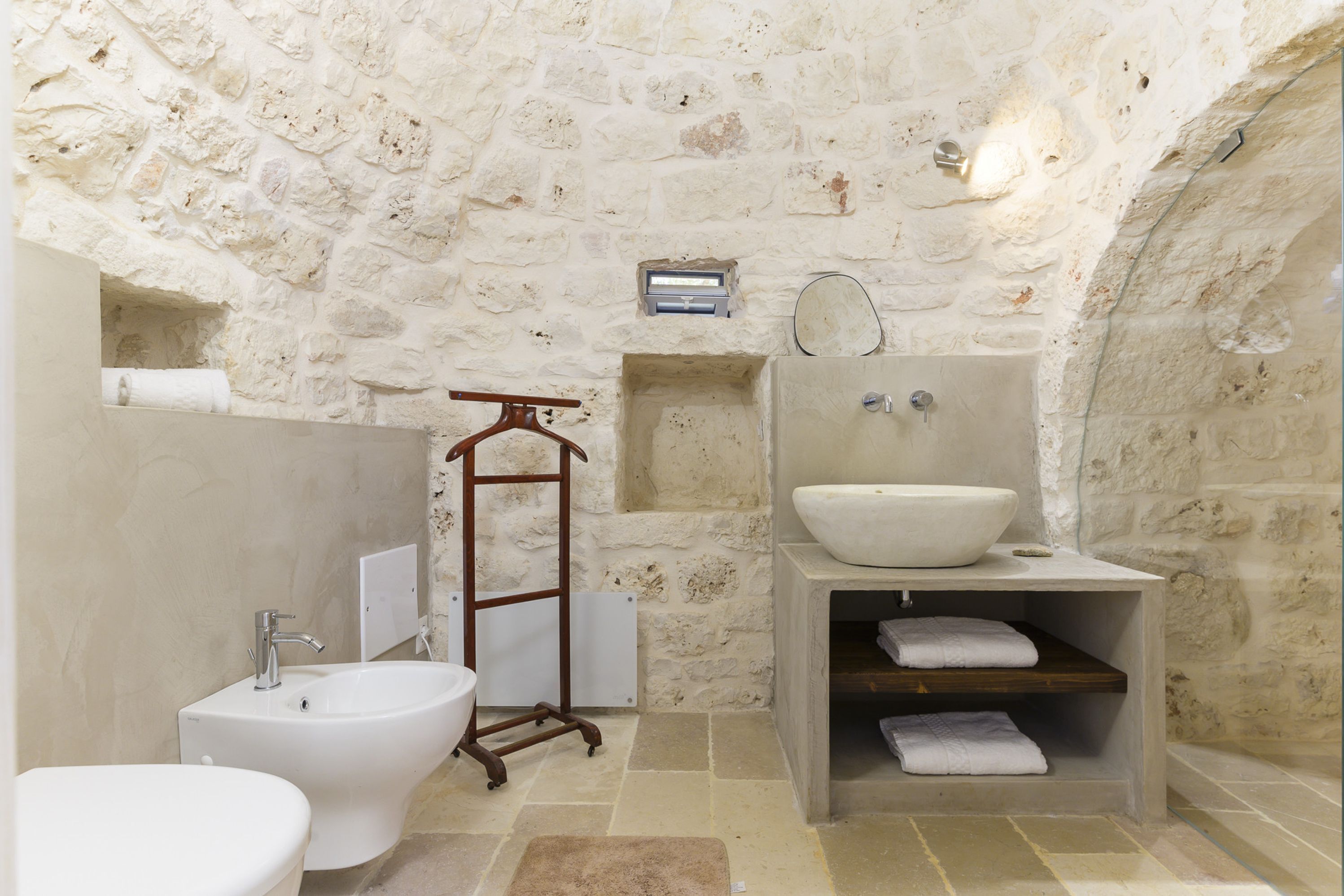 A bathroom with a stone wall, a bidet, a sink, and a towel rack.